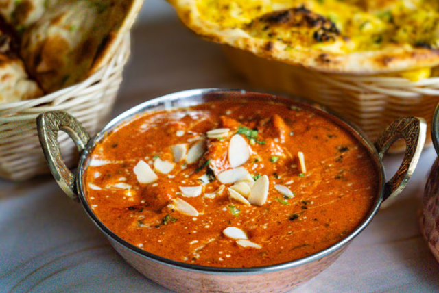 Bowl of butter chicken with almonds and naan bread in the background